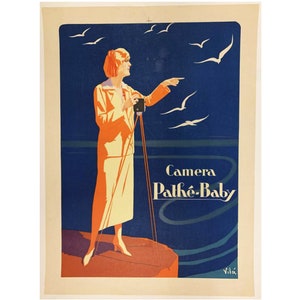 May include: A vintage poster advertising the Pathé-Baby camera. The poster features a woman in a yellow dress standing on a rock by the sea, holding a camera and pointing towards a flock of birds in the sky. The text "Camera Pathé-Baby" is printed in white on a blue background.