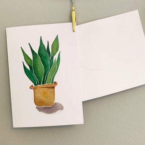 May include: A watercolour painting of a potted snake plant with green leaves and a brown pot. The plant is sitting on a white background.