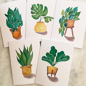 May include: Set of five watercolour illustrations of potted plants. Each illustration features a different type of plant with green leaves and a yellow pot. The illustrations are on white card stock.