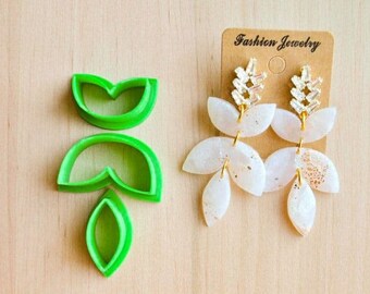 May include: A pair of white and gold fashion earrings with a leaf design, displayed on a brown tag that reads "Fashion Jewelry". Next to the earrings are three green leaf-shaped polymer clay cutters.