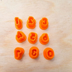 May include: Set of ten orange plastic cookie cutters shaped like the numbers 1 through 10.