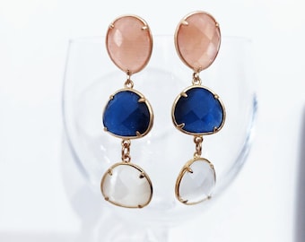 May include: A pair of dangle earrings with three round stones. The top stone is peach, the middle stone is blue, and the bottom stone is white.