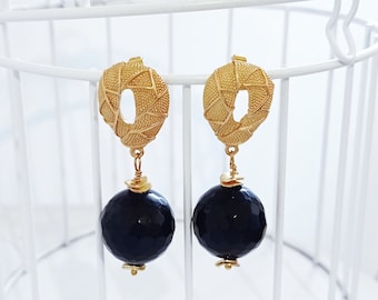 May include: Gold earrings with a geometric design and black gemstone drops.
