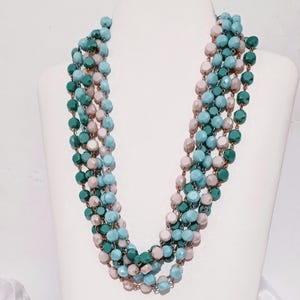 Può includere: Una collana multifilo realizzata con perline blu, verdi e beige. La collana è composta da più fili di perline intrecciati tra loro.