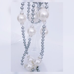 May include: A silver and white pearl necklace with large pearls. The necklace is draped over a wine glass.