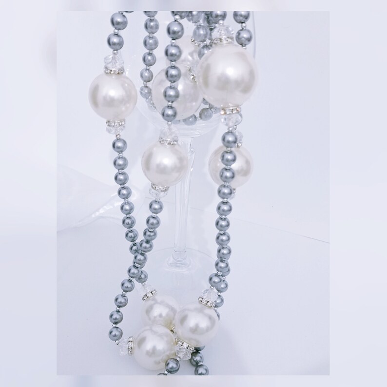 May include: A silver and white pearl necklace with large pearls. The necklace is draped over a wine glass.