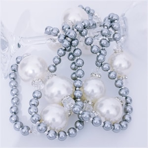 May include: A silver and white pearl necklace with large white pearls and smaller silver beads. The necklace is draped over a glass vase.