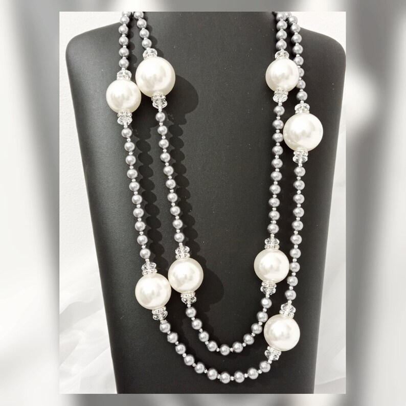 May include: A double strand pearl necklace with silver beads and large white faux pearls. The necklace is displayed on a black mannequin bust.