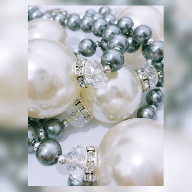 May include: A necklace made of large white pearls and smaller grey pearls. The pearls are strung on a silver chain and have clear crystal accents.