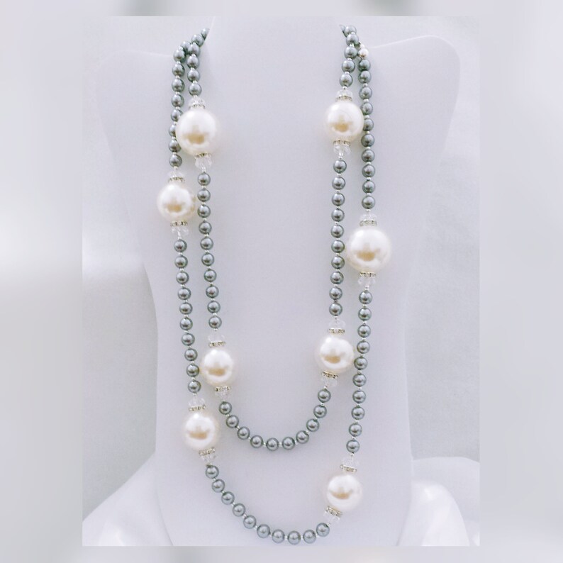 May include: A two-strand pearl necklace with grey beads and large white faux pearls. The necklace is displayed on a white mannequin bust.