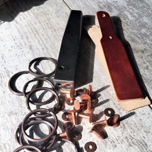 May include: A set of leather craft tools including a leather punch, a piece of leather, a set of copper rings, and copper rivets.