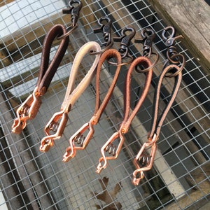 Puede incluir: Seis llaveros de cuero con cierres y anillas de metal de color cobre. Los llaveros son de varios tonos de marr&oacute;n, beige y crema.