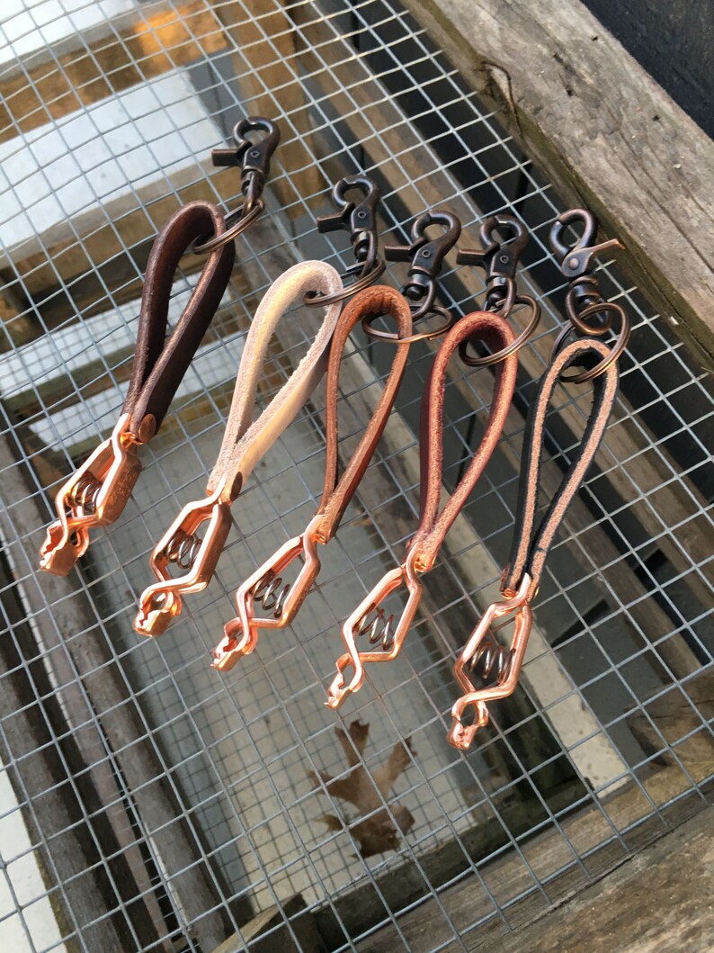 Puede incluir: Seis llaveros de cuero con cierres y anillas de metal de color cobre. Los llaveros son de varios tonos de marr&oacute;n, beige y crema.