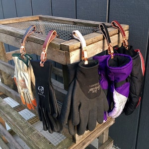 Puede incluir: Cinco pares de guantes colgados en un estante de madera. Los guantes son de varios colores y estilos, incluyendo negro, morado y gris. Todos los guantes est&aacute;n hechos de un material suave y c&oacute;modo y son perfectos para mantener las manos calientes en climas fr&iacute;os.