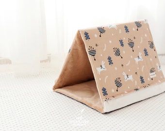 Peut inclure: Une tente pour animaux de compagnie beige et blanche avec un motif représentant des lapins blancs, des arbres bleus et des fleurs rayées noires et blanches. La tente a un intérieur doux et moelleux.