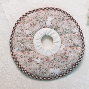 Puede incluir: Un collar de recuperaci&oacute;n para mascotas beige con un estampado floral y de conejitos. El collar tiene un centro blanco y un borde a cuadros marr&oacute;n y blanco. La tela es suave y acolchada.