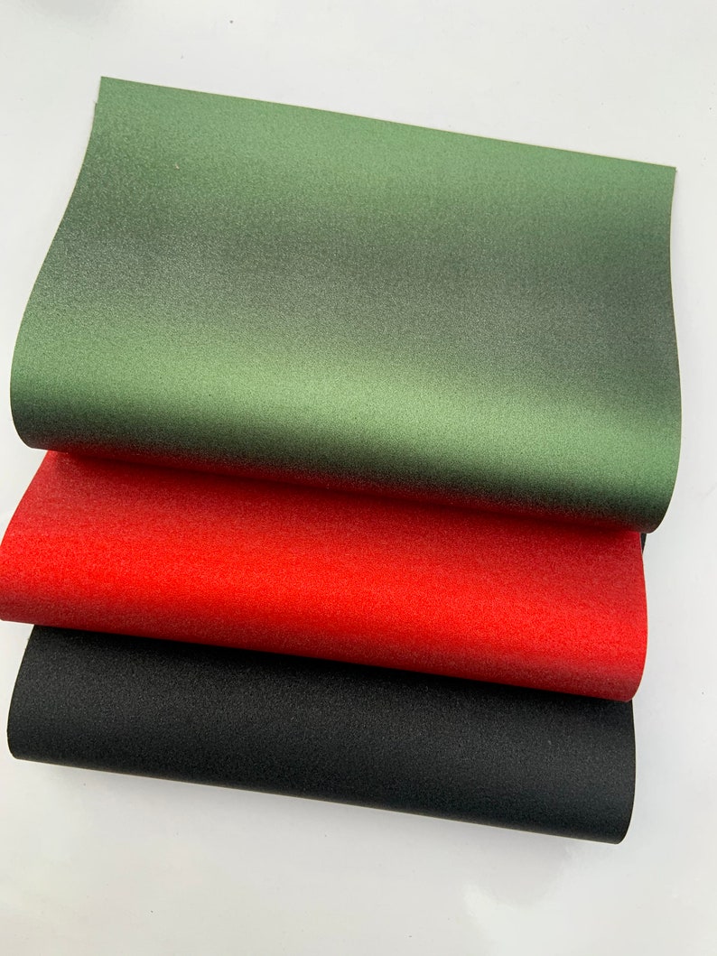 Op de afbeelding: Drie vellen getextureerd papier in groen, rood en zwart. Het groene vel ligt bovenaan, gevolgd door het rode en dan het zwarte. Het papier heeft een subtiele, gespikkelde uitstraling.