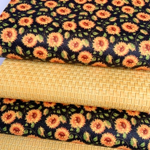 May include: Two pieces of fabric, one with a woven pattern and the other with a sunflower print. The sunflower fabric is black with yellow sunflowers and green leaves. The woven fabric is a light beige.