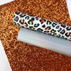 May include: Two sheets of faux leather fabric. One sheet is a brown glitter fabric. The other sheet is a white fabric with a rainbow leopard print.