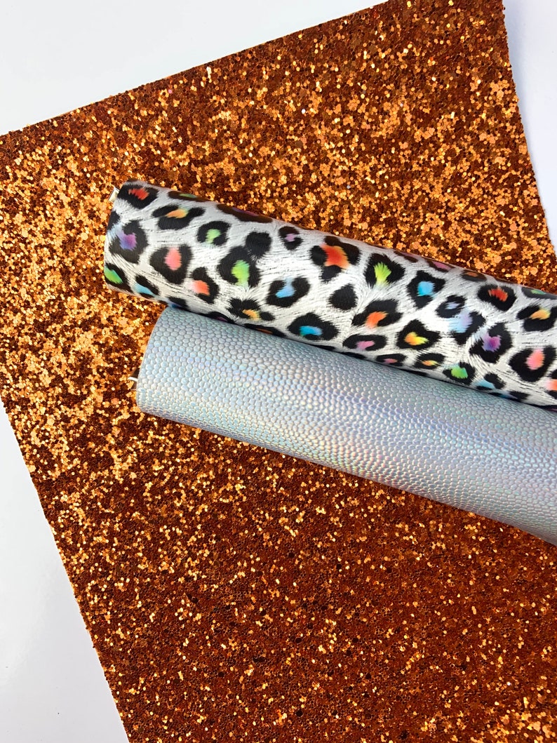 May include: Two sheets of faux leather fabric. One sheet is a brown glitter fabric. The other sheet is a white fabric with a rainbow leopard print.