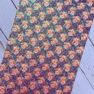 May include: A sheet of glitter fabric with a repeating floral pattern. The flowers are pink and gold, set against a dark blue background. The glitter adds a shimmering effect, suitable for crafts and embellishments.