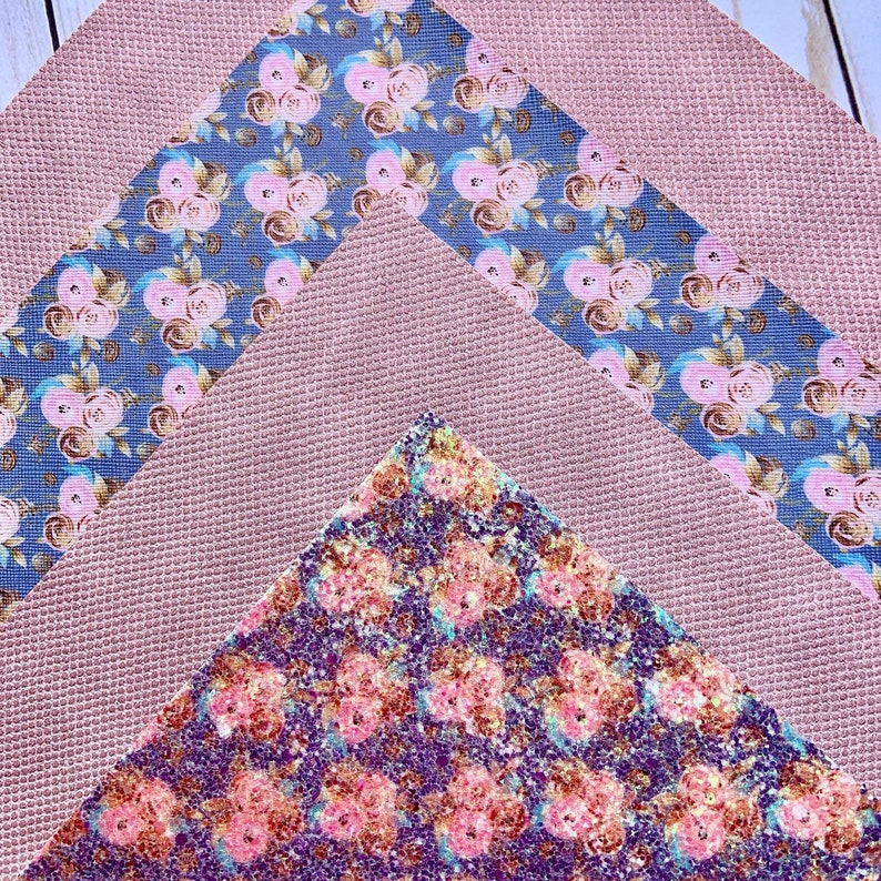 May include: An overhead shot displays three pieces of fabric. A textured, mauve-colored fabric forms the base. A blue fabric with pink floral patterns and a glittery, purple fabric with pink floral patterns are layered on top.
