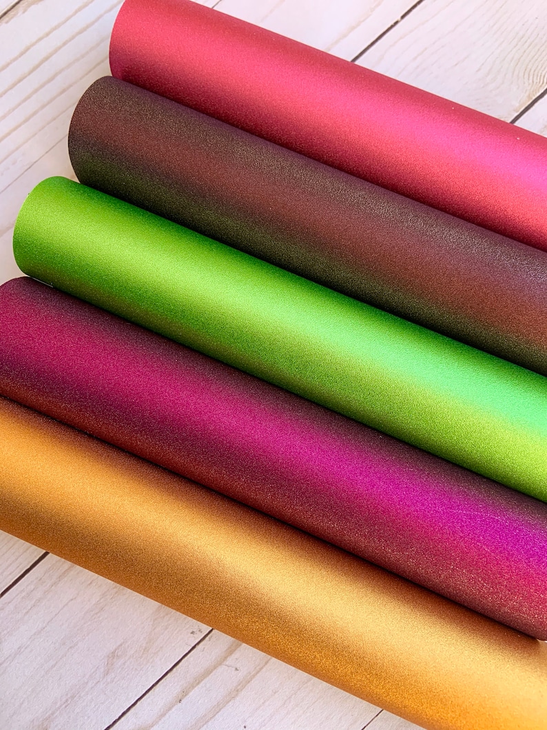 K&ouml;nnte beinhalten: F&uuml;nf Rollen irisierendes Glitzer-Vinyl in verschiedenen Farben: Gold, Burgunder, Lila, Gr&uuml;n und Braun. Das Vinyl ist strukturiert und hat einen metallischen Glanz.