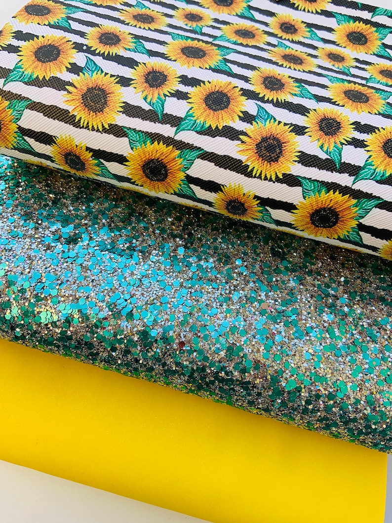 May include: Three sheets of fabric: a black and white striped fabric with a sunflower pattern, a green glitter fabric, and a solid yellow fabric.
