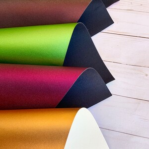 K&ouml;nnte beinhalten: F&uuml;nf Bl&auml;tter metallisches Papier in verschiedenen Farben, in der Mitte gefaltet und &uuml;bereinander gestapelt. Die Farben sind rot, braun, gr&uuml;n, burgunderrot und gold.