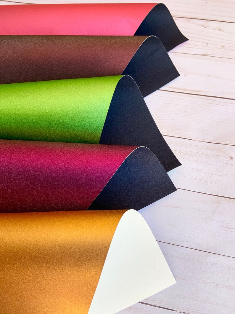 K&ouml;nnte beinhalten: F&uuml;nf Bl&auml;tter metallisches Papier in verschiedenen Farben, in der Mitte gefaltet und &uuml;bereinander gestapelt. Die Farben sind rot, braun, gr&uuml;n, burgunderrot und gold.