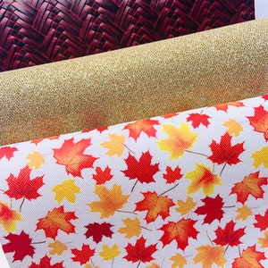 May include: Three rolls of fabric with different patterns. The top roll is a dark red woven fabric. The middle roll is a gold glitter fabric. The bottom roll is a white fabric with a red and yellow maple leaf pattern.