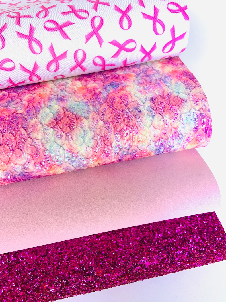 May include: Four sheets of pink patterned faux leather. The top sheet has a white background with pink ribbon designs. The second sheet has a pink, purple, and white tie-dye pattern with a subtle glitter finish. The third sheet is a solid light pink. The bottom sheet is a bright pink glitter fabric.