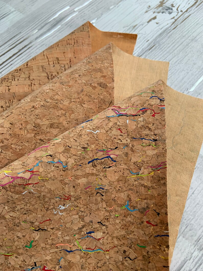 May include: Three sheets of cork fabric, one plain, one with a subtle texture, and one with colorful lines. The cork fabric is a natural material with a brown color.