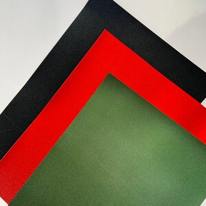 Op de afbeelding: Een diagonale compositie van drie vellen getextureerd papier in zwart, rood en olijfgroen. Het zwarte vel ligt bovenop, gevolgd door rood en groen, wat een visueel contrast cre&euml;ert. De textuur is goed zichtbaar.