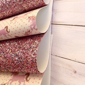 May include: Three sheets of pink glitter fabric with a white unicorn print. The fabric is folded in a stack.