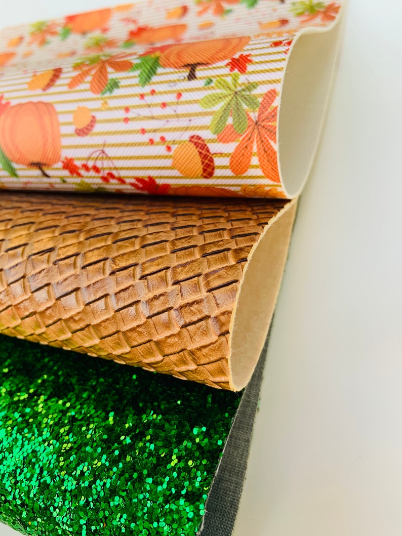 May include: Close-up of three different textured sheets. The top sheet has a fall-themed pattern with pumpkins, leaves, and acorns. The middle sheet is brown with a woven pattern. The bottom sheet is covered in green glitter.
