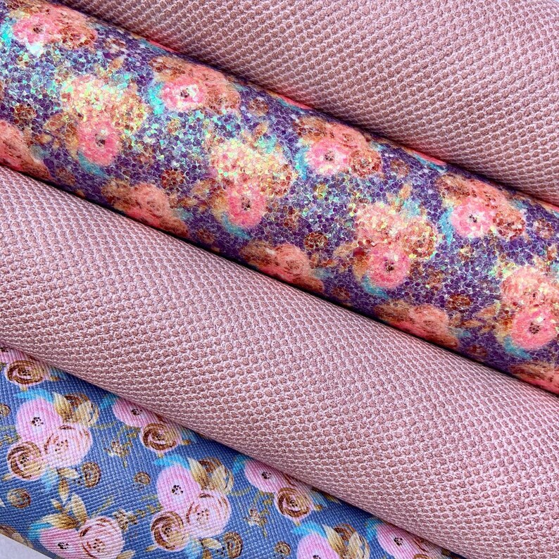 May include: Close-up of several rolls of fabric. Two rolls are a solid, textured, light pink color. The other two rolls have floral patterns in shades of pink, blue, and purple. The fabric appears to be faux leather or vinyl.