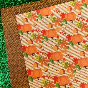 May include: An assortment of textured craft papers. Includes a green glitter sheet, a brown embossed sheet, and a sheet with a pumpkin and fall leaf pattern on a striped background. Ideal for fall-themed crafts.