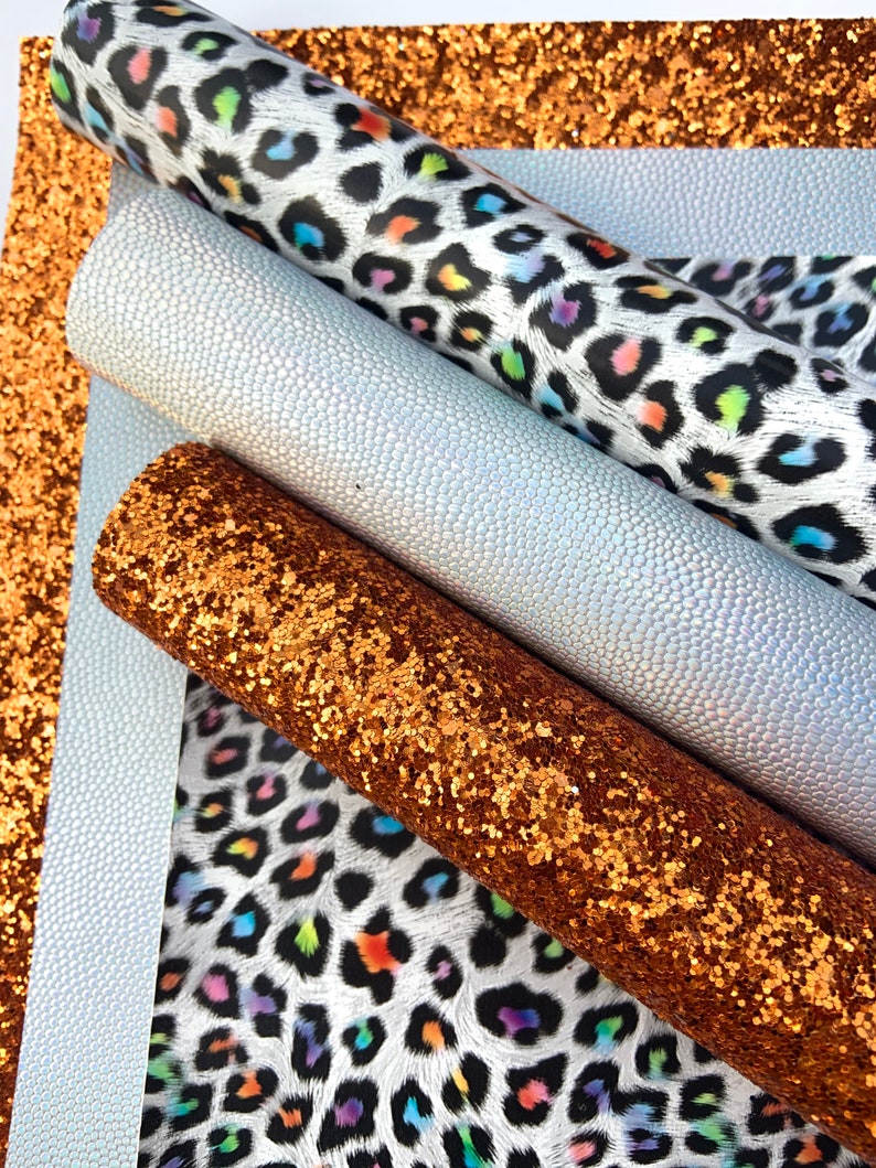 May include: A set of four craft supplies featuring a white and black leopard print with rainbow accents, a white iridescent faux leather, and a copper glitter fabric.