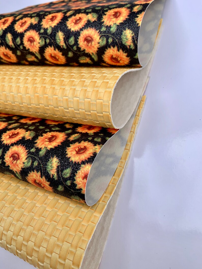 May include: Three rolls of fabric, one with a woven pattern and two with a sunflower print on a black background.