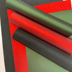 Op de afbeelding: Overzicht van vellen en opgerolde buizen van getextureerd papier in zwart, rood en groen. De opgerolde buizen zijn diagonaal over de afbeelding geplaatst, met de vellen eronder. Geschikt voor knutselen.