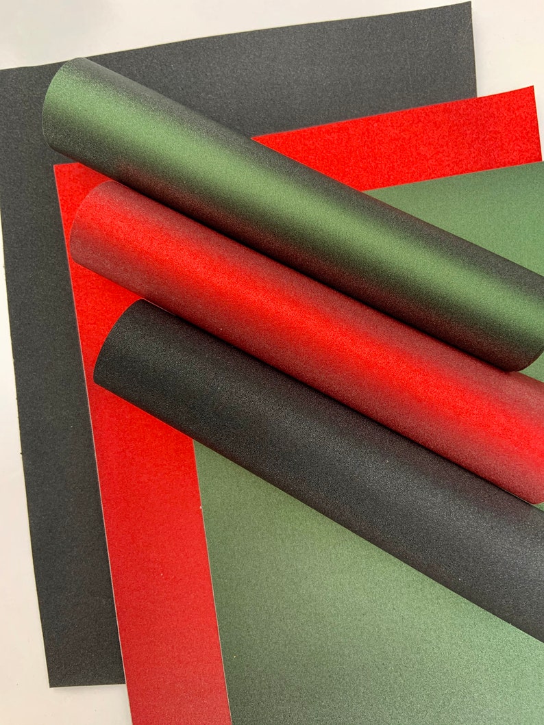 Op de afbeelding: Overzicht van vellen en opgerolde buizen van getextureerd papier in zwart, rood en groen. De opgerolde buizen zijn diagonaal over de afbeelding geplaatst, met de vellen eronder. Geschikt voor knutselen.