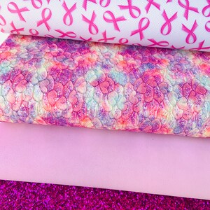 May include: Four sheets of pink and purple patterned faux leather. The top sheet features a white background with pink ribbon designs. The second sheet has a pink, purple, and white tie-dye pattern. The third sheet is a solid light pink. The bottom sheet is a sparkly pink glitter.