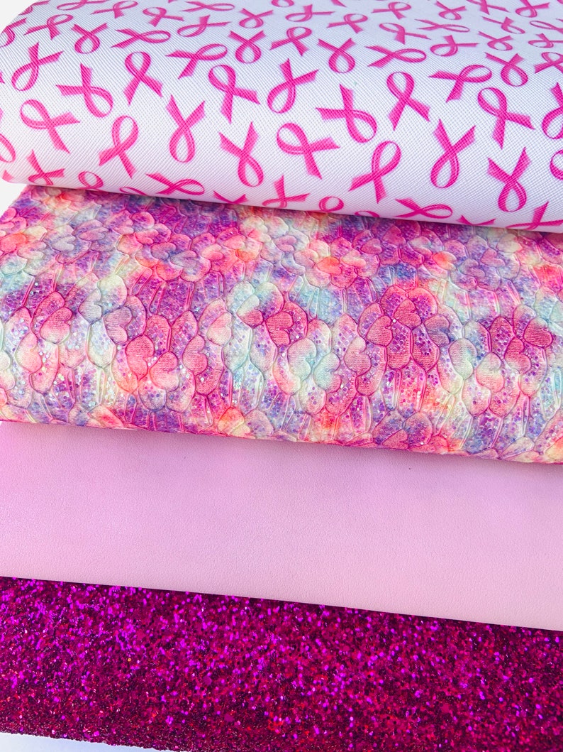 May include: Four sheets of pink and purple patterned faux leather. The top sheet features a white background with pink ribbon designs. The second sheet has a pink, purple, and white tie-dye pattern. The third sheet is a solid light pink. The bottom sheet is a sparkly pink glitter.