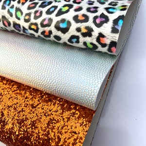 May include: Three different fabric swatches stacked on top of each other. The top swatch is a white fabric with a black and rainbow leopard print. The middle swatch is a light gray fabric with a subtle iridescent texture. The bottom swatch is a copper colored fabric with a glitter finish.