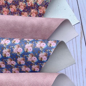 May include: Four sheets of decorative faux leather in various patterns. The top sheet has a glitter floral design with pink and gold flowers on a dark blue background. The second and fourth sheets are a textured pink. The third sheet has a floral pattern with pink roses on a blue background.