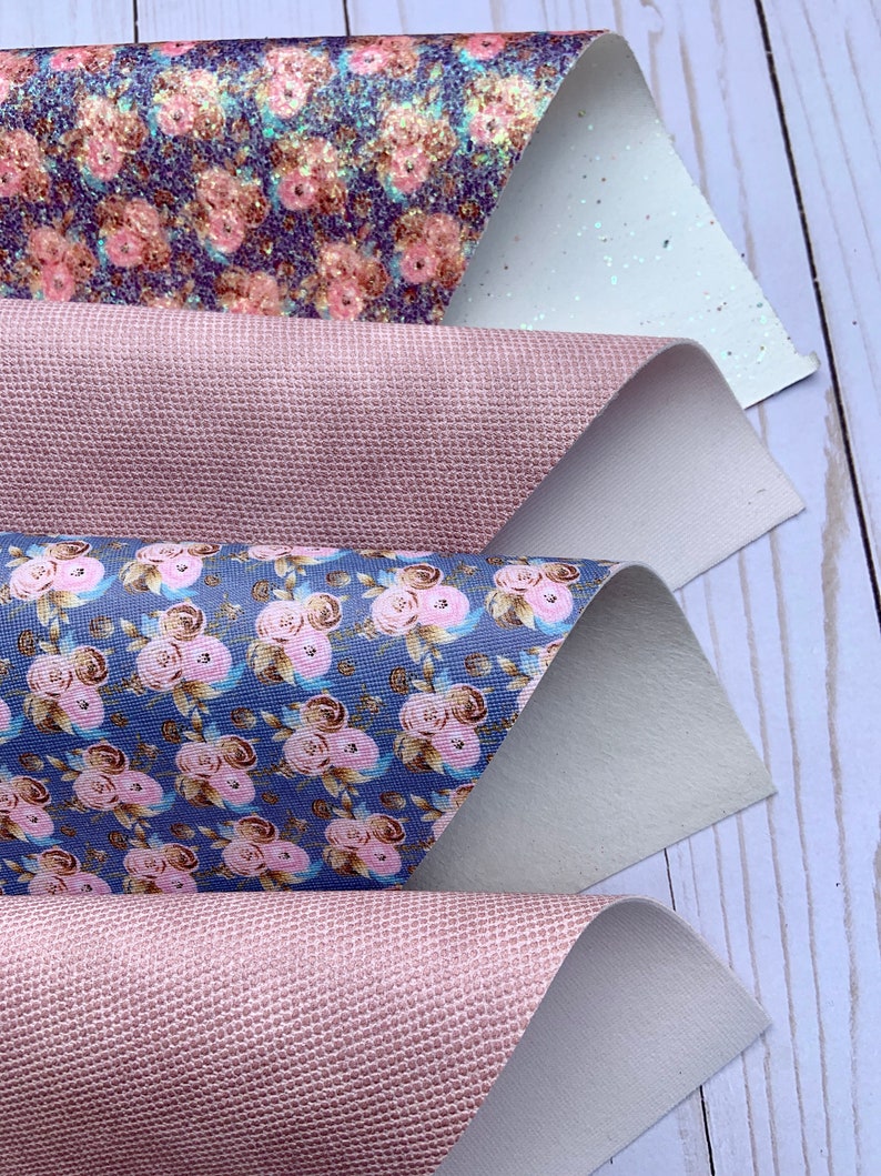May include: Four sheets of decorative faux leather in various patterns. The top sheet has a glitter floral design with pink and gold flowers on a dark blue background. The second and fourth sheets are a textured pink. The third sheet has a floral pattern with pink roses on a blue background.