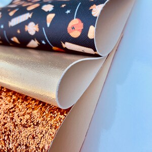 May include: A stack of four fabric swatches. The top swatch is black with a white and orange candy pattern. The second swatch is a metallic gold. The third swatch is a light beige. The bottom swatch is a sparkly copper.