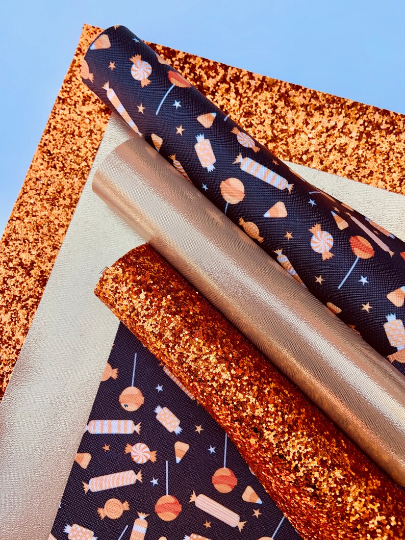 May include: A set of four fabric sheets in various textures and colors. The sheets include a black fabric with a white and orange candy pattern, a gold glitter fabric, a copper glitter fabric, and a gold metallic fabric.