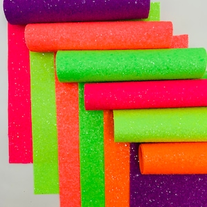 Pu&ograve; includere: Un rotolo di tessuto glitterato in vari colori neon, tra cui rosa, arancione, verde e viola. Il tessuto &egrave; arrotolato e le estremit&agrave; sono visibili.